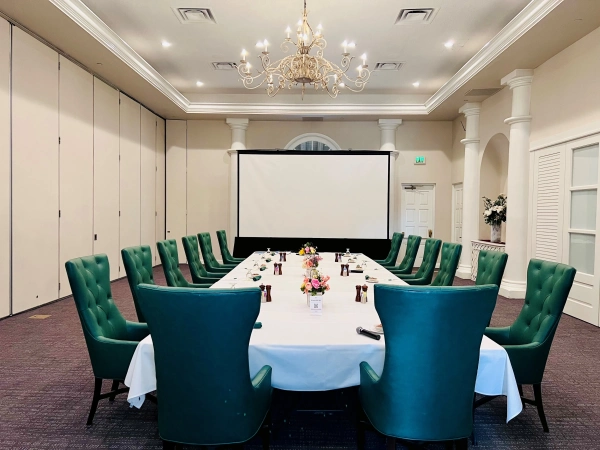 Boardroom table with teal chairs under a chandelier
